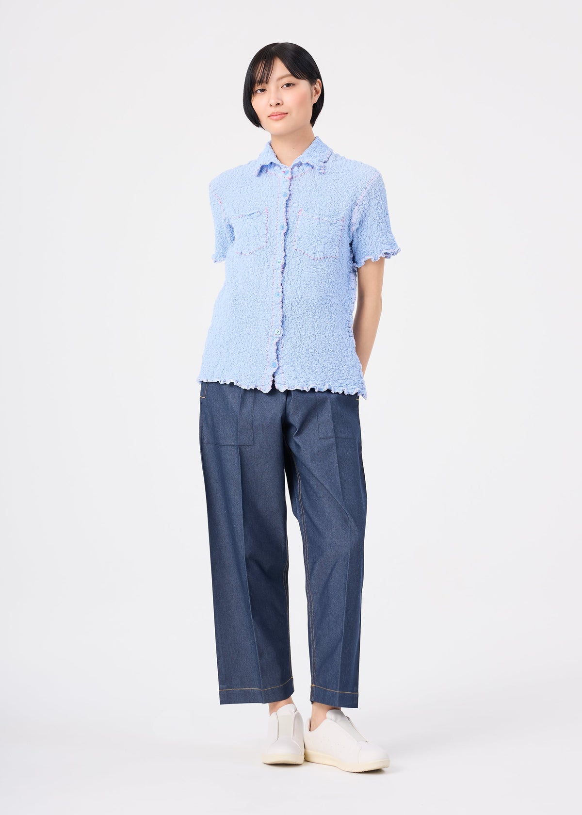 A person with short black hair wears the CAULIFLOWER COLOR 1 top by me ISSEY MIYAKE, paired with wide-leg blue pants and white slip-on shoes, standing against a plain white background. view 7 of 7