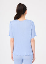 A woman with long dark hair in a ponytail is shown from behind, wearing the SEE-THROUGH CREPE COLOR set by me ISSEY MIYAKE—light blue, product-dyed sheer top and matching pants—against a plain white background.