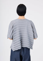 A person with short black hair is seen from behind, wearing the me ISSEY MIYAKE ACCORDION SEE-THROUGH CREPE light gray, garment-dyed textured short-sleeve top with horizontal stripes and dark blue wide-leg pants against a plain white background.