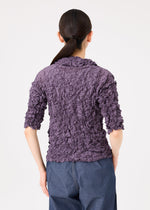 A person with long dark hair in a ponytail is seen from the back, wearing the MERINGUE TOP by me ISSEY MIYAKE with three-quarter sleeves and blue pants against a plain background.
