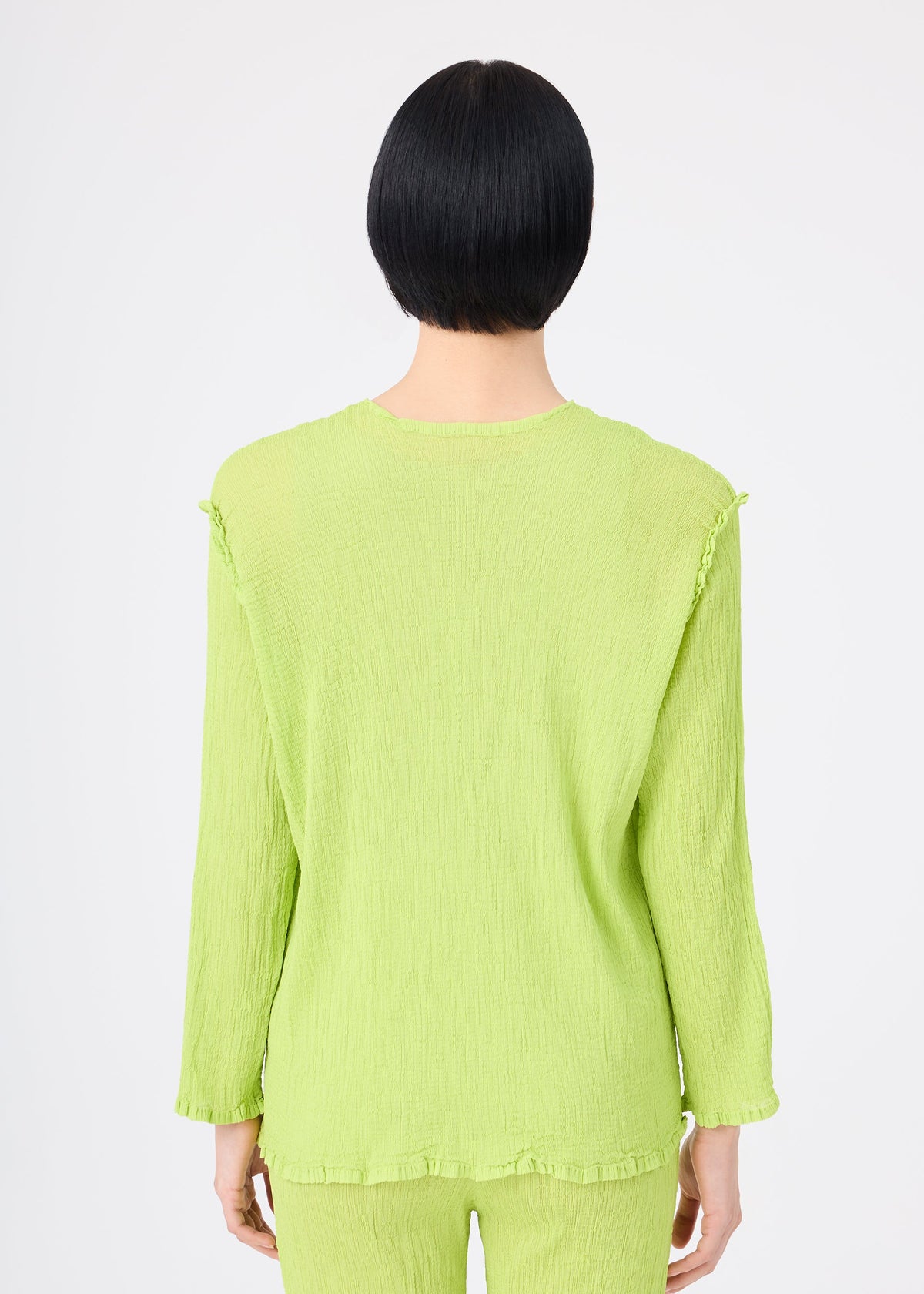 A person with short black hair is seen from behind, wearing a lime green SEE-THROUGH CREPE COLOR set by me ISSEY MIYAKE. The long-sleeved, textured top and matching pants are product-dyed. The background is plain white. view 6 of 7