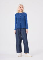 A person with light hair wears the me ISSEY MIYAKE STRIPE CAULIFLOWER textured blue long-sleeve top, paired with wide-leg denim pants and white shoes, standing against a plain light background.