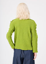Person with shoulder-length blonde hair wears the ROUND CAULIFLOWER cardigan by me ISSEY MIYAKE in bright green, paired with dark blue pants, shown from the back against a plain light background.