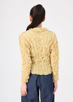 A person with long dark hair in a high ponytail wears the MERINGUE TOP by me ISSEY MIYAKE in light yellow and dark blue pants, standing with their back to the camera against a plain white background.