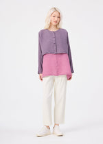 A person with light blonde hair wears the me ISSEY MIYAKE POLYCOTTON CREPE purple and pink layered button-up top, cream pants, and white slip-ons, standing against a plain white background.