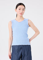 A woman with straight black hair wears the CAULIFLOWER COLOR 1 sleeveless top by me ISSEY MIYAKE in light blue, styled with dark blue pants. She stands against a plain white background, her expression neutral.