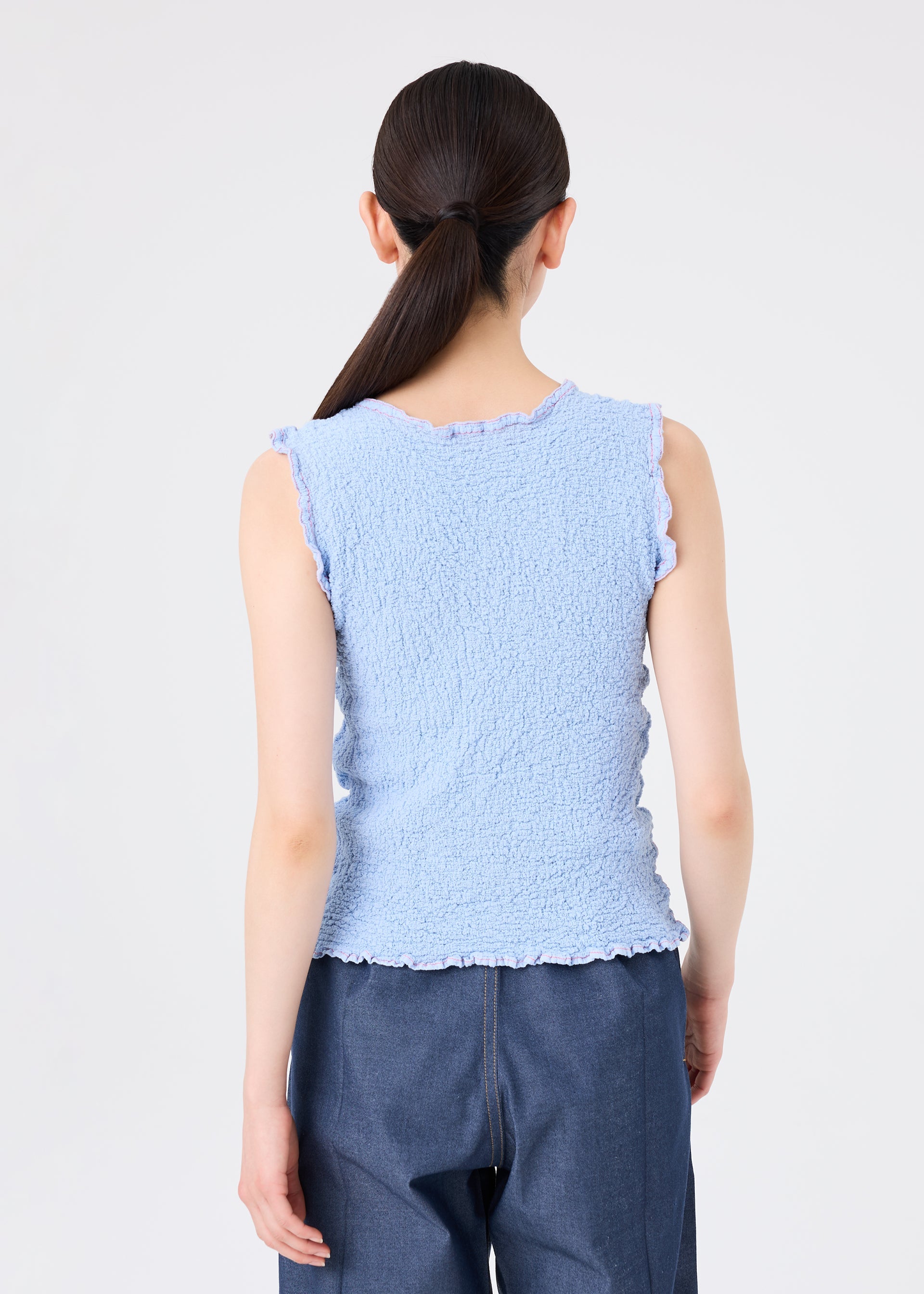 Zoomed view A person with long dark hair in a low ponytail is shown from the back, wearing the CAULIFLOWER COLOR 1 top by me ISSEY MIYAKE and dark blue denim pants against a plain light background.
