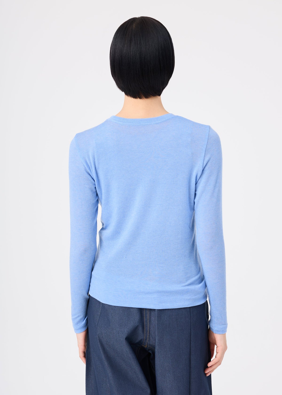 Zoomed view A person with short black hair, wearing the WOOL MIX JERSEY by me ISSEY MIYAKE in light blue and dark blue jeans, stands facing away from the camera against a plain white background.