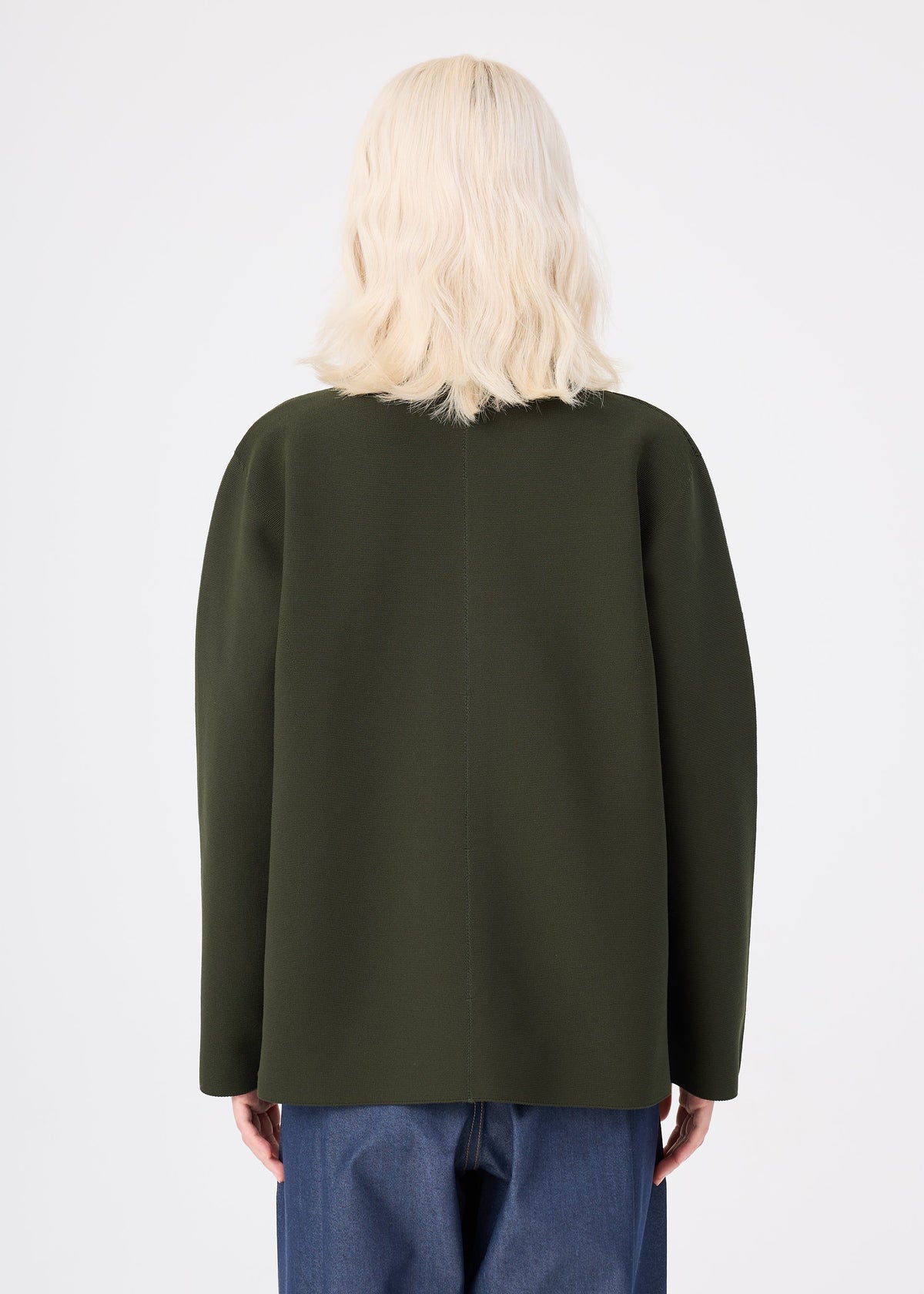 A person with shoulder-length blonde hair is seen from behind, wearing the me ISSEY MIYAKE SOLID KNIT in olive green and blue jeans against a plain white background. view 7 of 8