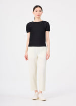 A woman with straight dark hair pulled back and a neutral expression wears the FINE KNIT PLEATS top by me ISSEY MIYAKE, paired with lightweight white straight pants and white shoes, standing against a white background.