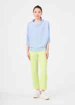 A woman faces forward against a white background, wearing me ISSEY MIYAKE's FINE KNIT PLEATS COLOR 1—a lightweight light blue top with three-quarter sleeves—paired with pale yellow straight pants and white slip-on shoes.