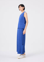 A person stands sideways against a plain white background, wearing the me ISSEY MIYAKE FINE KNIT PLEATS BOTTOM 1—wide, pleated knit pants in blue—paired with a sleeveless blue top and white sneakers.