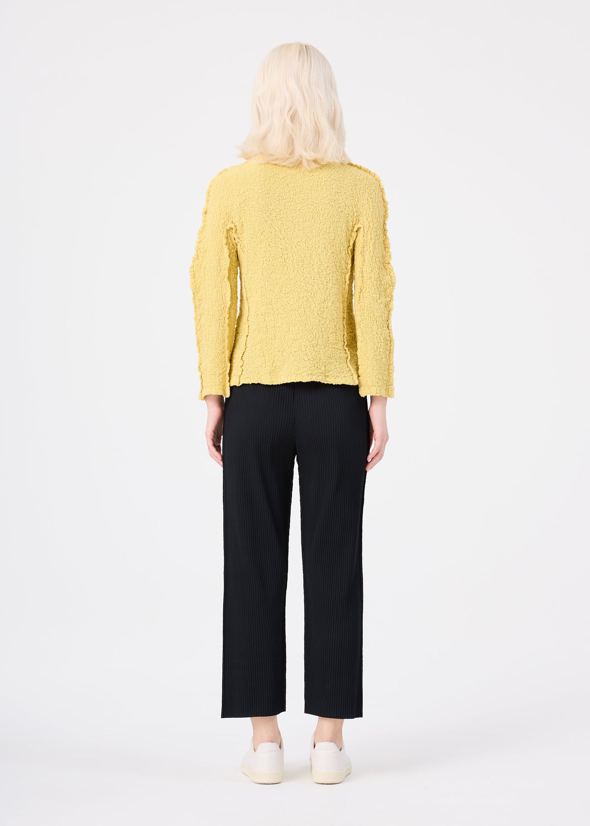 Zoomed view Person with shoulder-length blond hair wearing a textured yellow long-sleeve top, MIX FINE KNIT PLEATS BOTTOM by me ISSEY MIYAKE, and white shoes, standing with their back to the camera against a plain white background.