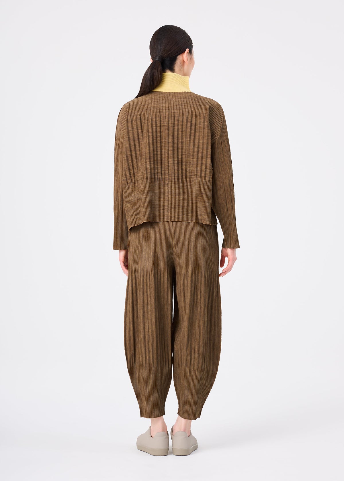 A person stands facing away against a white background, wearing me ISSEY MIYAKE MIX FINE KNIT PLEATS BOTTOM and a matching loose brown top, with light shoes and hair tied back. view 7 of 7