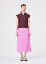 A woman stands against a plain white background, facing forward with her arms relaxed by her sides. She is wearing a short-sleeve maroon top, the FINE KNIT PLEATS BOTTOM 1 skirt in pink by me ISSEY MIYAKE, and beige shoes.