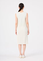A woman with dark hair in a low ponytail stands facing away, wearing a sleeveless, knee-length cream FINE KNIT PLEATS dress from me ISSEY MIYAKE and white slip-on shoes against a plain white background.