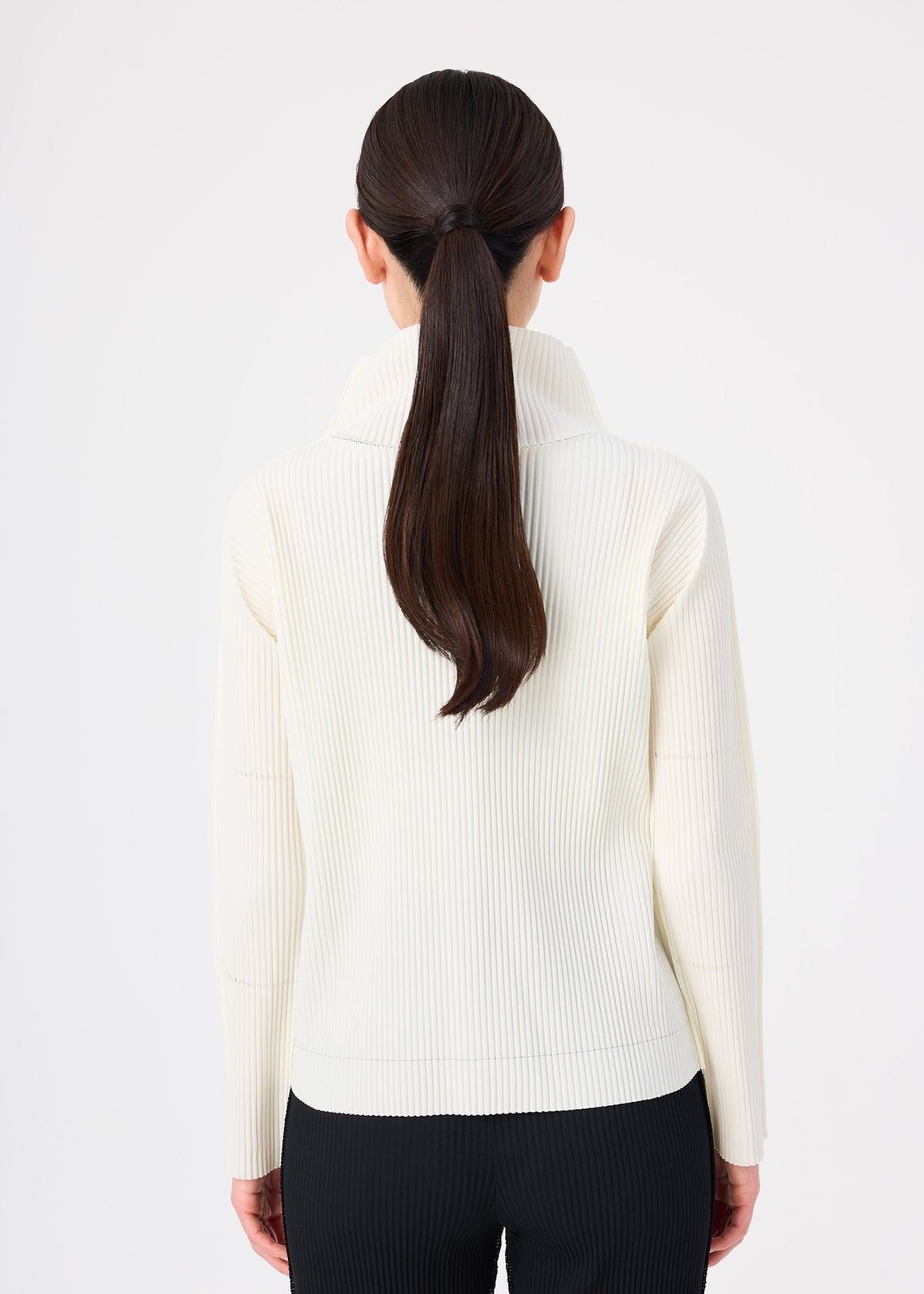 A woman with long, straight dark hair in a low ponytail is seen from behind, wearing the FINE KNIT PLEATS top by me ISSEY MIYAKE and black pants against a plain white background. view 5 of 6