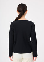 A person with long dark hair in a low ponytail is shown from the back, wearing the me ISSEY MIYAKE FINE KNIT PLEATS black ribbed long-sleeved top and white pants against a plain white background.
