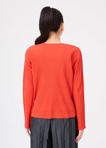 A person with long dark hair in a ponytail is seen from behind against a plain white background, wearing the me ISSEY MIYAKE FINE KNIT PLEATS COLOR 2 top in red and high-waisted gray pants.