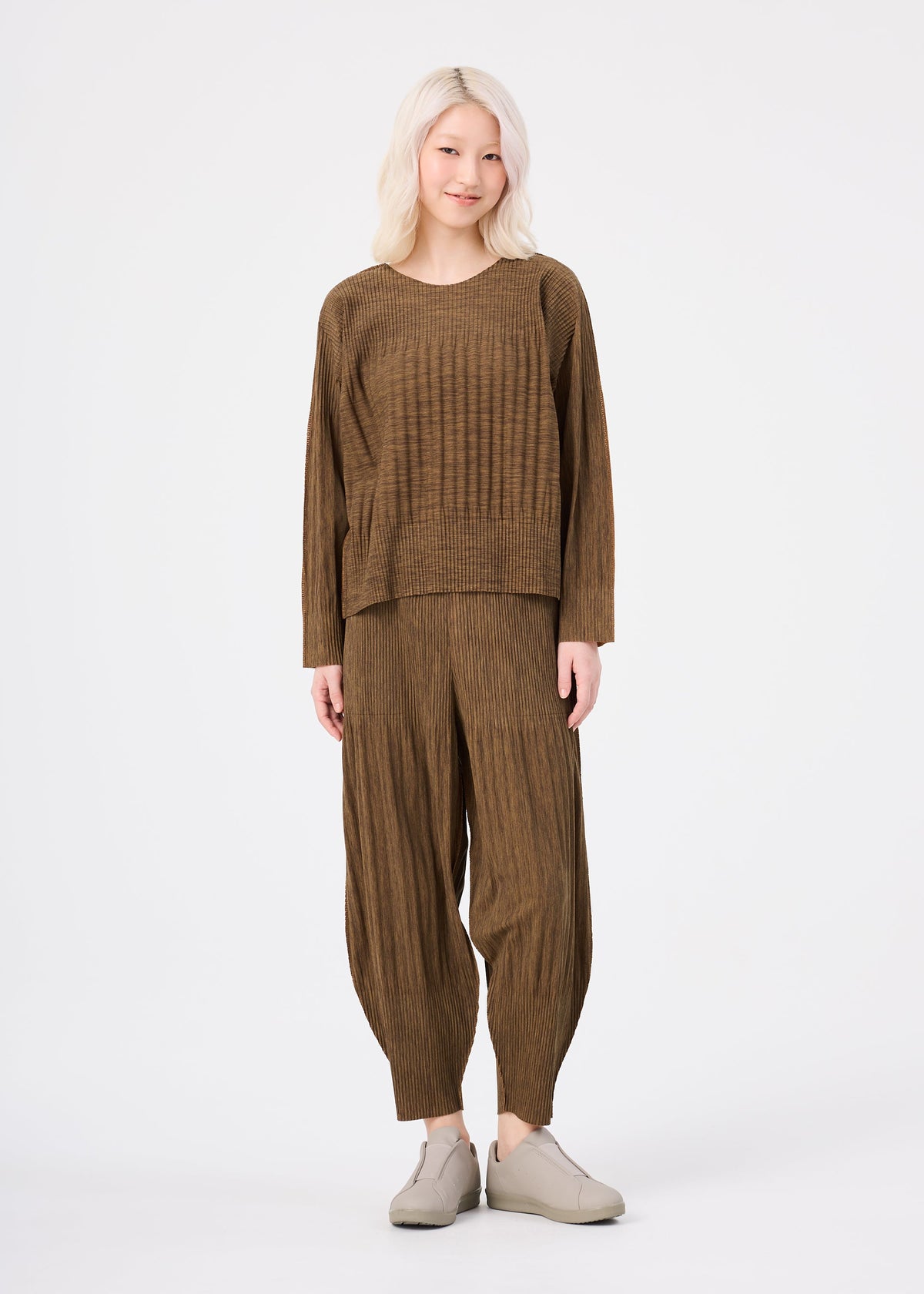 Zoomed view A person with light blonde hair wears the me ISSEY MIYAKE MIX FINE KNIT PLEATS set—loose long-sleeved top and matching wide-legged pants—with light slip-on shoes, standing against a plain white background.