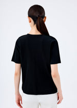A person with long dark hair in a low ponytail is seen from behind wearing the me ISSEY MIYAKE FINE KNIT PLEATS black short-sleeved top and white pants against a plain light background.