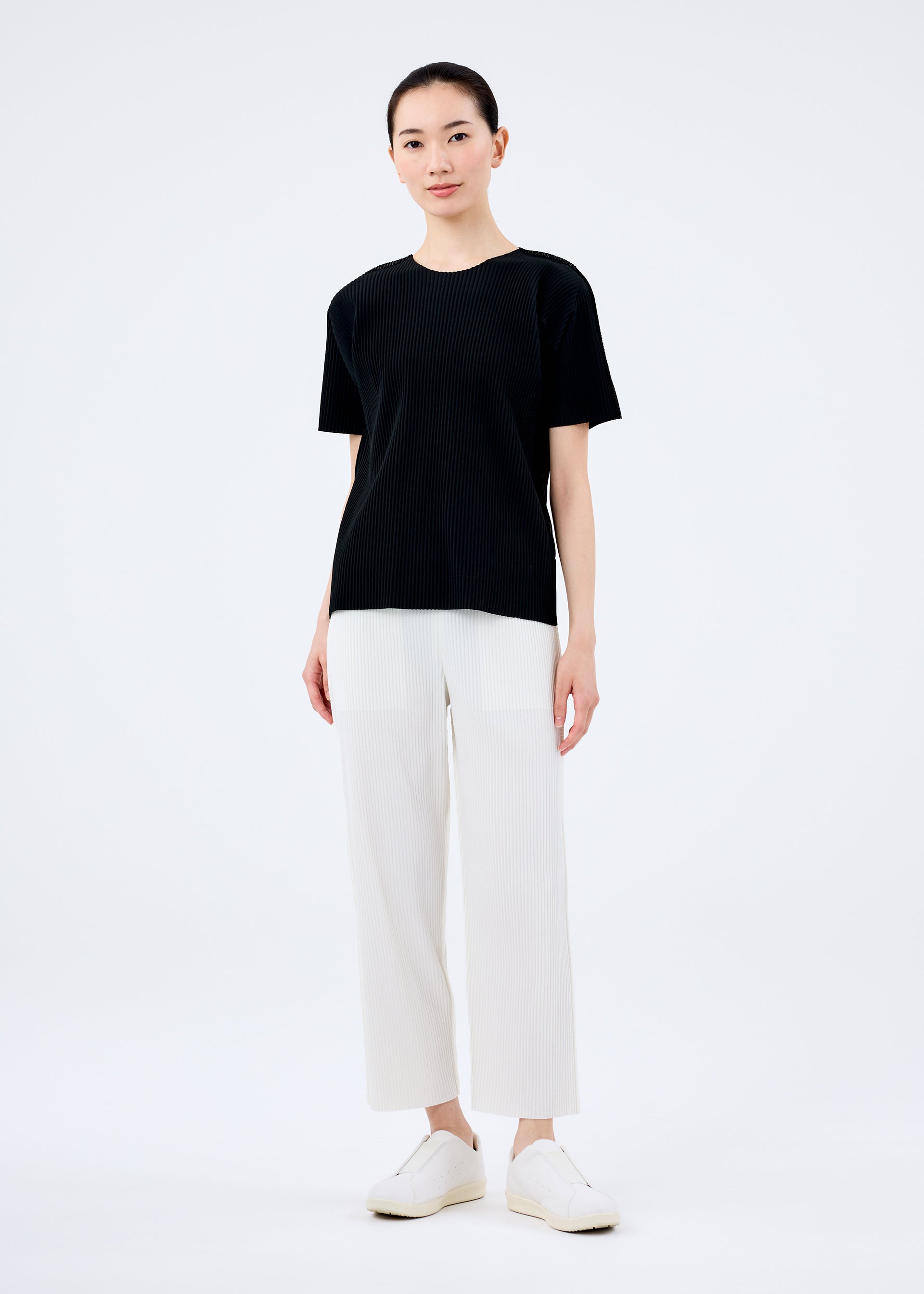 Zoomed view A person stands facing forward against a plain white background, wearing the FINE KNIT PLEATS top by me ISSEY MIYAKE, paired with white straight-leg pants and white shoes.