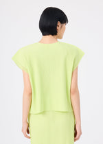 A person with short black hair, seen from behind, wears the light green MESH PLEATS top and matching skirt by me ISSEY MIYAKE, featuring fine knit pleats, against a plain white background.