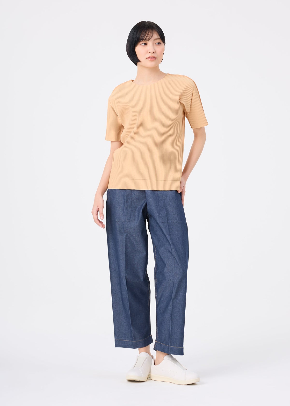 A person with short black hair wears the FINE KNIT PLEATS COLOR 1 top by me ISSEY MIYAKE, paired with loose blue jeans and white slip-on shoes, standing against a plain white background. view 8 of 8