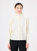 A woman with straight dark hair tied back models the me ISSEY MIYAKE FINE KNIT PLEATS cream high-neck cardigan with black pants against a plain white background.