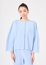 A woman with long dark hair tied back wears the light blue MESH PLEATS set from me ISSEY MIYAKE, featuring a pleated cardigan and matching pants. She stands against a plain white background, smiling gently at the camera.