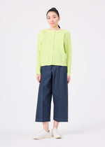 A woman faces forward against a white background, wearing the me ISSEY MIYAKE FINE KNIT PLEATS COLOR 1 cardigan in light green, paired with wide-leg dark blue jeans and white slip-on shoes.
