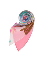 The PLEATS STOLE / NY by me ISSEY MIYAKE, in pink with colorful floral and abstract patterns, is rolled into a spiral on a white background.