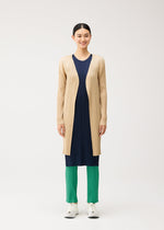 A person wearing a long, beige pleated mid-length coat over a navy pleated dress and green pleated trousers from the PLEATS PLEASE ISSEY MIYAKE NEW COLORFUL BASICS 5 collection, finished with white sneakers.