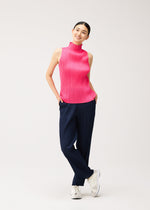 A smiling person wears a brightly colored pink sleeveless pleated mock-neck NEW COLORFUL BASICS 5 top and navy straight pants with white sneakers.