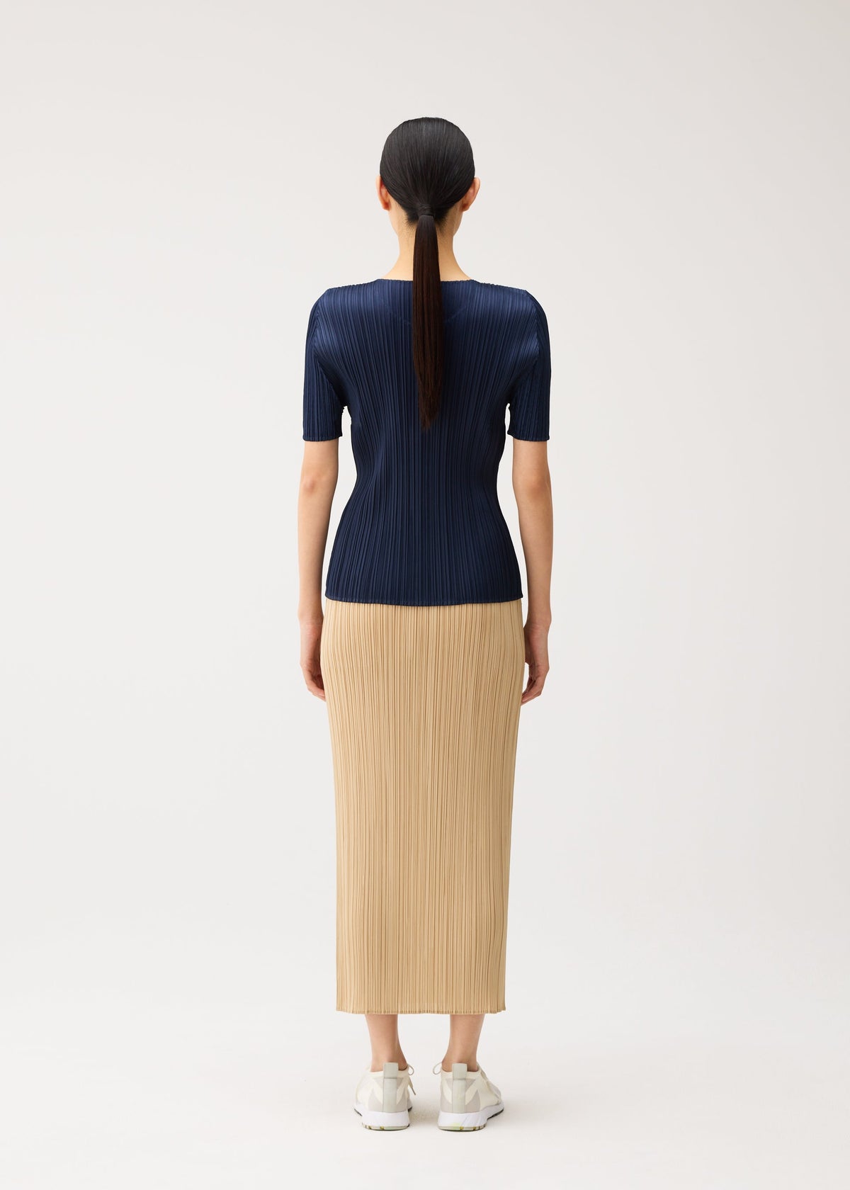 Zoomed view A person seen from behind wears a navy short-sleeved pleated top and a long tan pleated skirt from the NEW COLORFUL BASICS 5 collection by PLEATS PLEASE ISSEY MIYAKE.