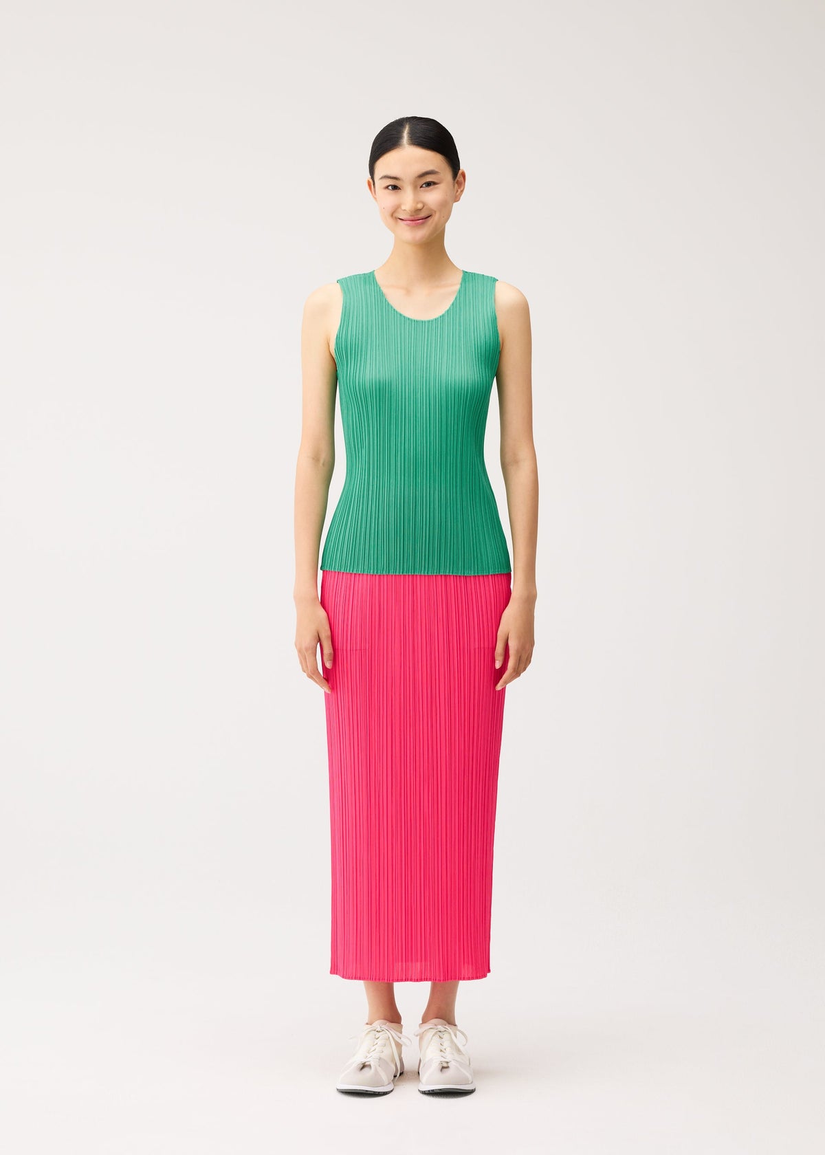 Zoomed view A model wearing a PLEATS PLEASE ISSEY MIYAKE NEW COLORFUL BASICS 5 green, round-neck sleeveless top and a long pink pleated skirt with white sneakers.