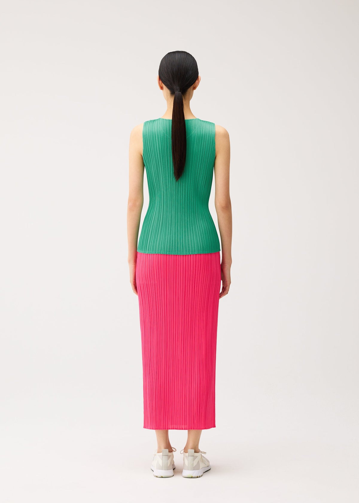 Back view of a person wearing a NEW COLORFUL BASICS 5 sleeveless green pleated top and a long pink pleated skirt with white sneakers. view 9 of 10