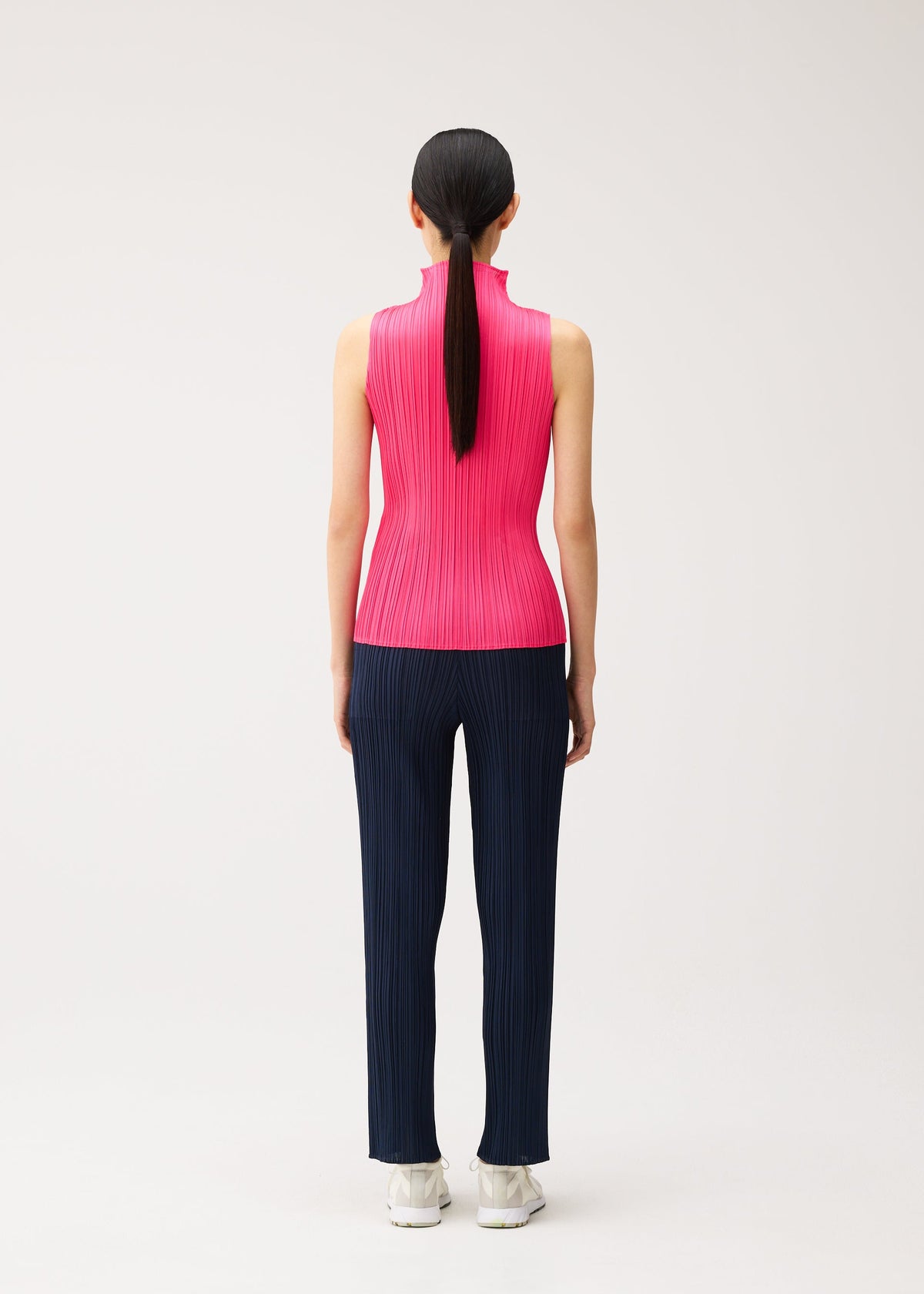 Back view of a person wearing a bright pink sleeveless high-neck shirt and dark blue pleated trousers from the NEW COLORFUL BASICS 5 collection by PLEATS PLEASE ISSEY MIYAKE, an easy to style ensemble. view 9 of 10