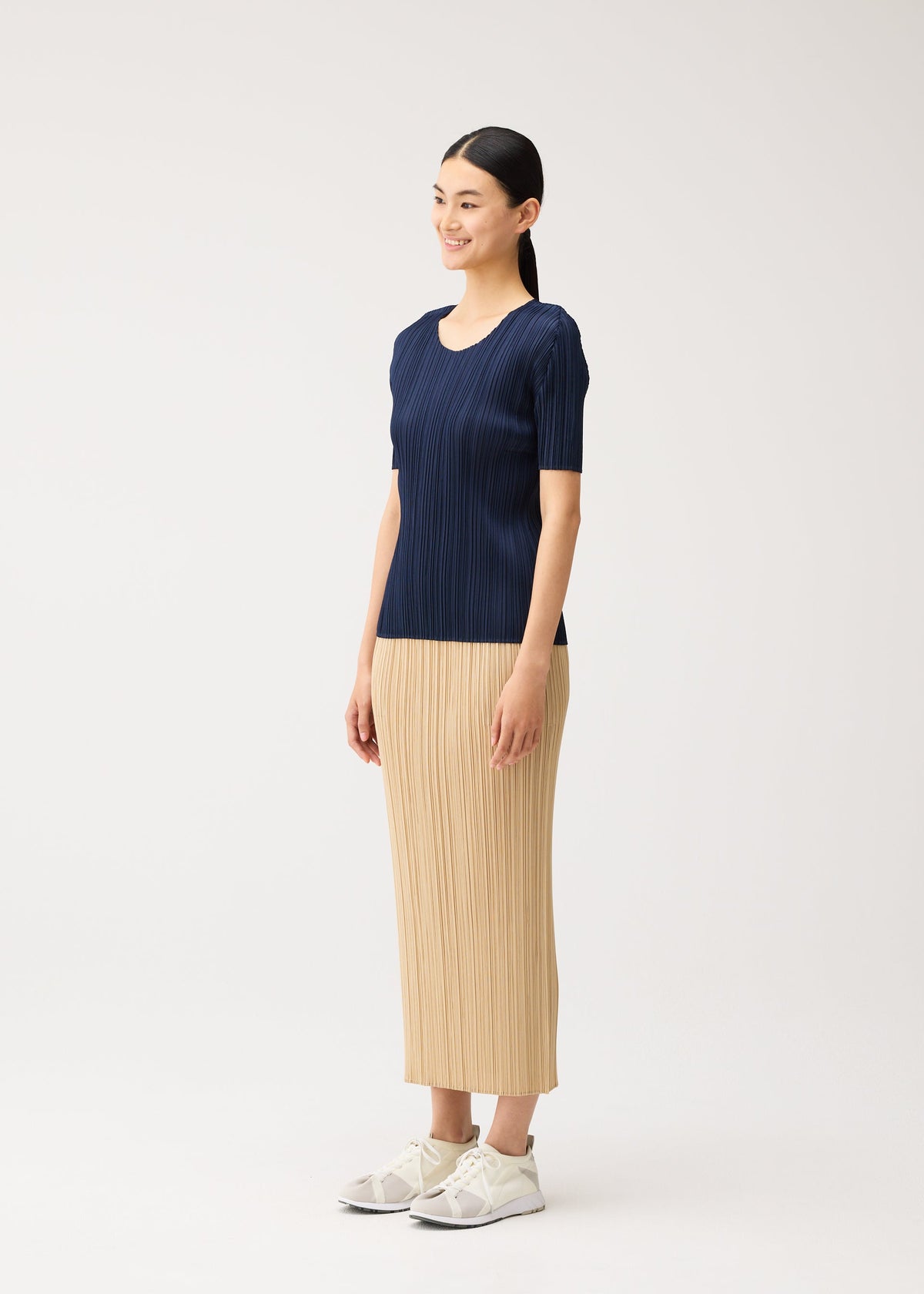 Zoomed view A person wearing a NEW COLORFUL BASICS 5 navy blue pleated short-sleeved top and a tan pleated midi skirt with light-colored sneakers.