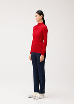 A person in profile wearing a NEW COLORFUL BASICS 5 long-sleeved pleated mock-neck top, navy blue pleated trousers, and white sneakers.