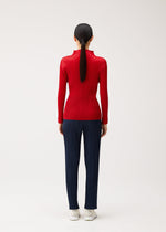 A person viewed from behind wearing a bright, high-neck red long-sleeved pleated top and navy pleated trousers from the NEW COLORFUL BASICS 5 collection by PLEATS PLEASE ISSEY MIYAKE, finished with white sneakers.