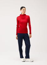 A woman wears a NEW COLORFUL BASICS 5 long-sleeved, high-neck pleated red top and navy pleated trousers, paired with white sneakers.