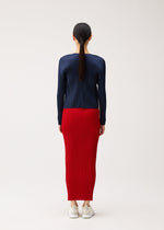 Seen from behind, a person wears a PLEATS PLEASE ISSEY MIYAKE NEW COLORFUL BASICS 5 navy blue long-sleeved pleated top and a bright red ankle-length pleated skirt, paired with white sneakers.