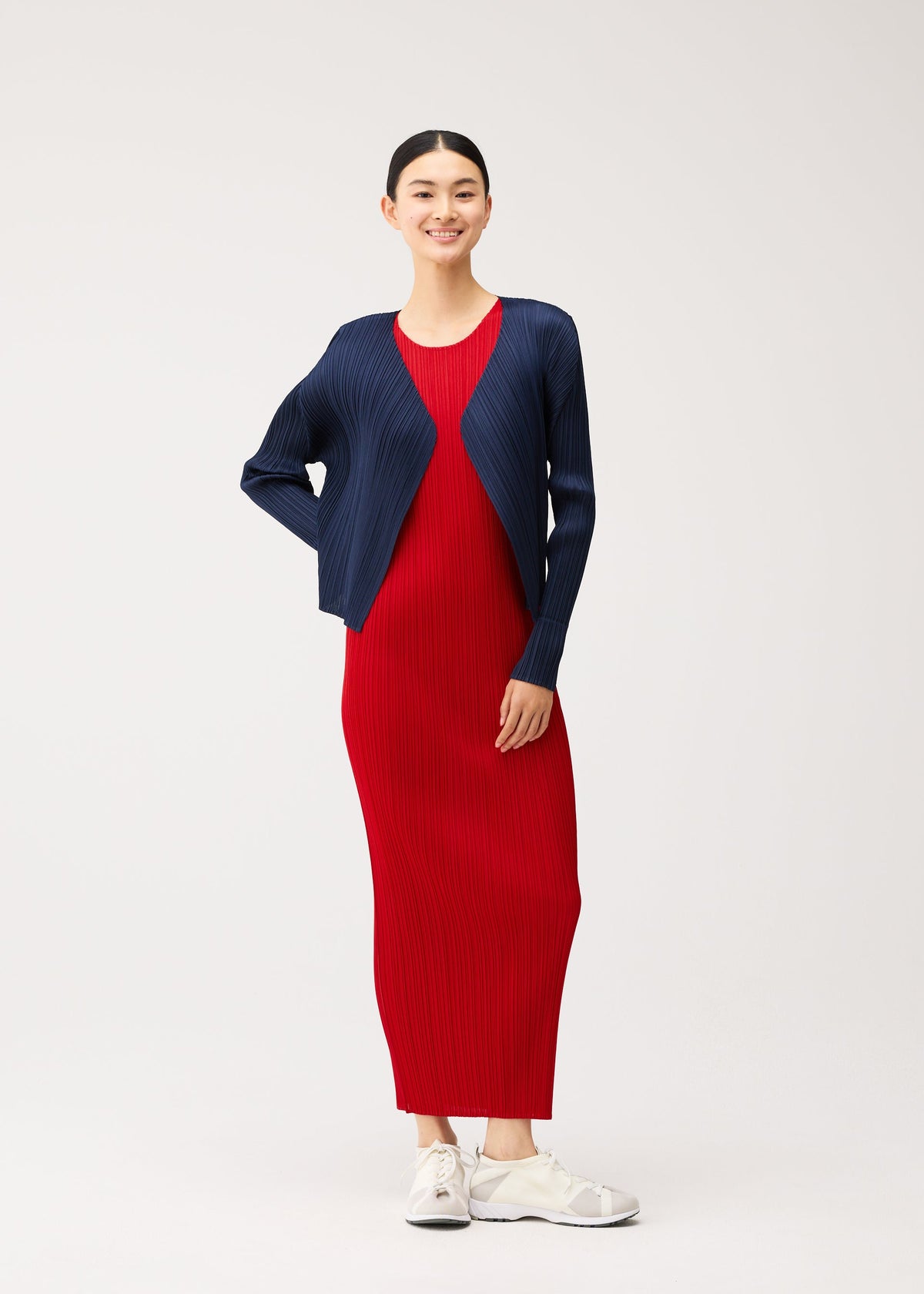 A person wearing a short, navy pleated cardigan from the NEW COLORFUL BASICS 5 collection over an easy-to-style red maxi dress and white sneakers. view 10 of 10