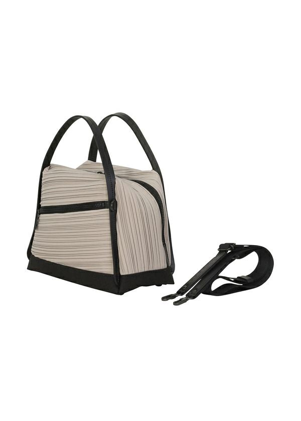 Zoomed view The BIAS PLEATS BAG by PLEATS PLEASE ISSEY MIYAKE features structured pleats in light grey fabric with black leather handles, base, and zipper. Includes an attached adjustable black shoulder strap. Shown on a white background.