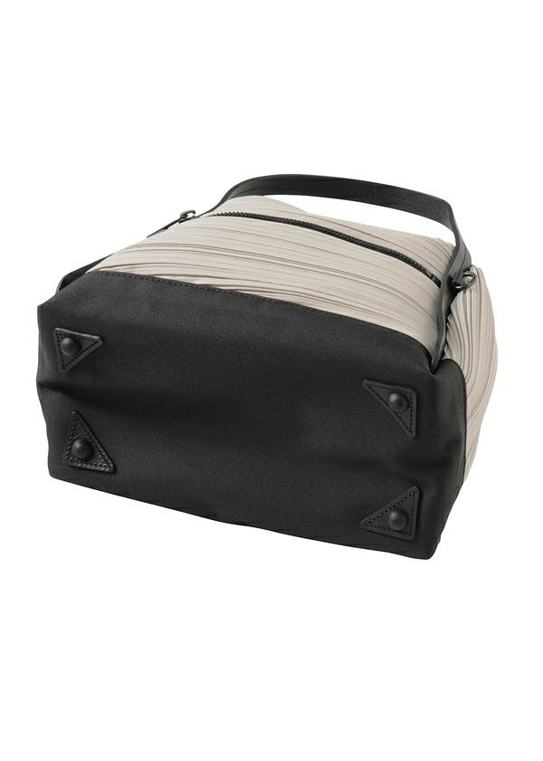 The BIAS PLEATS BAG by PLEATS PLEASE ISSEY MIYAKE is a rectangular shoulder bag with a black base, light beige sides, black handle, attached strap, top zipper, and four black protective studs on the bottom. view 6 of 8