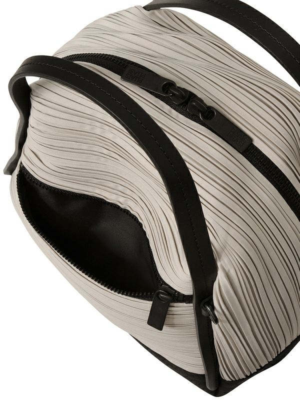 A close-up of the BIAS PLEATS BAG by PLEATS PLEASE ISSEY MIYAKE shows its beige, ribbed pleats, black handles, and partially open black zipper revealing a black interior. The shoulder bag comes with an attached strap for versatile carrying. view 7 of 8