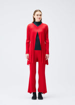 A woman faces forward in the OLE! pleated long red cardigan and matching pants by PLEATS PLEASE ISSEY MIYAKE over a black turtleneck, paired with black lace-up shoes, set against a plain white background.