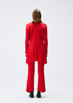 A person with shoulder-length brown hair stands facing away, wearing the OLE! long-sleeve red tunic and matching pleated pants by PLEATS PLEASE ISSEY MIYAKE, paired with black shoes, against a plain white background.