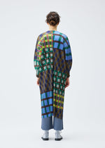 A person faces away, wearing the HARMONY coat by PLEATS PLEASE ISSEY MIYAKE, featuring a bold geometric print in blue, green, yellow, and red over pleated blue pants and gray shoes against a white background.